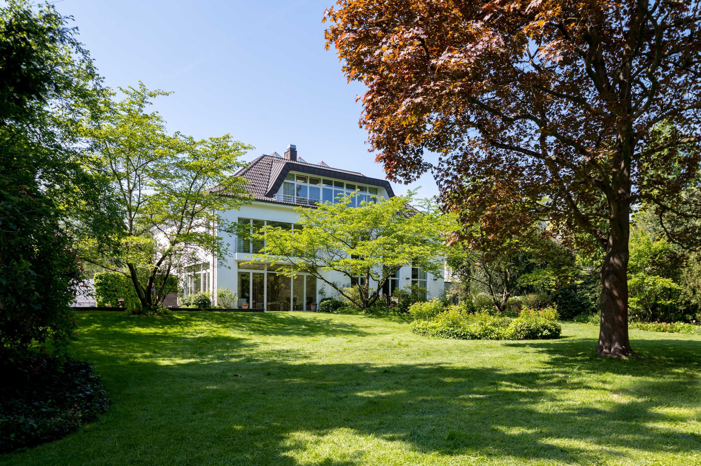 Immobilie Architekturfotografie eines Hauses in einem grünen Parkgelände. Viele Bäume und Wiesen.