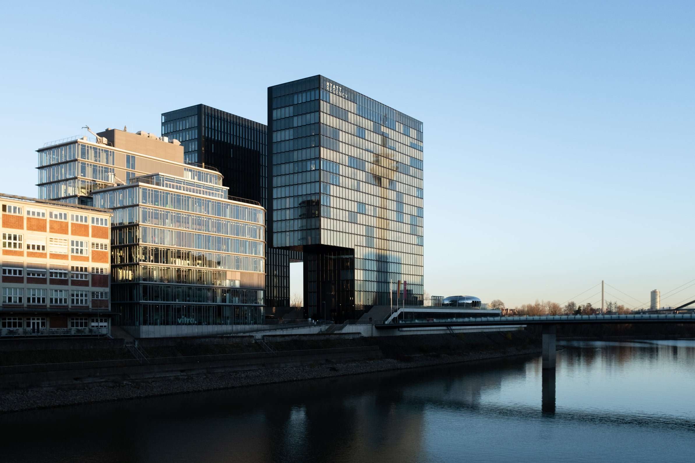 Blick vom Medienhafen quer zum Hochhaus Hyatt. Der Rheinturm spiegelt sich in der Fassade des Hotels. Rechts fließt der Rhein in Düsseldorf. Sonnenuntergang