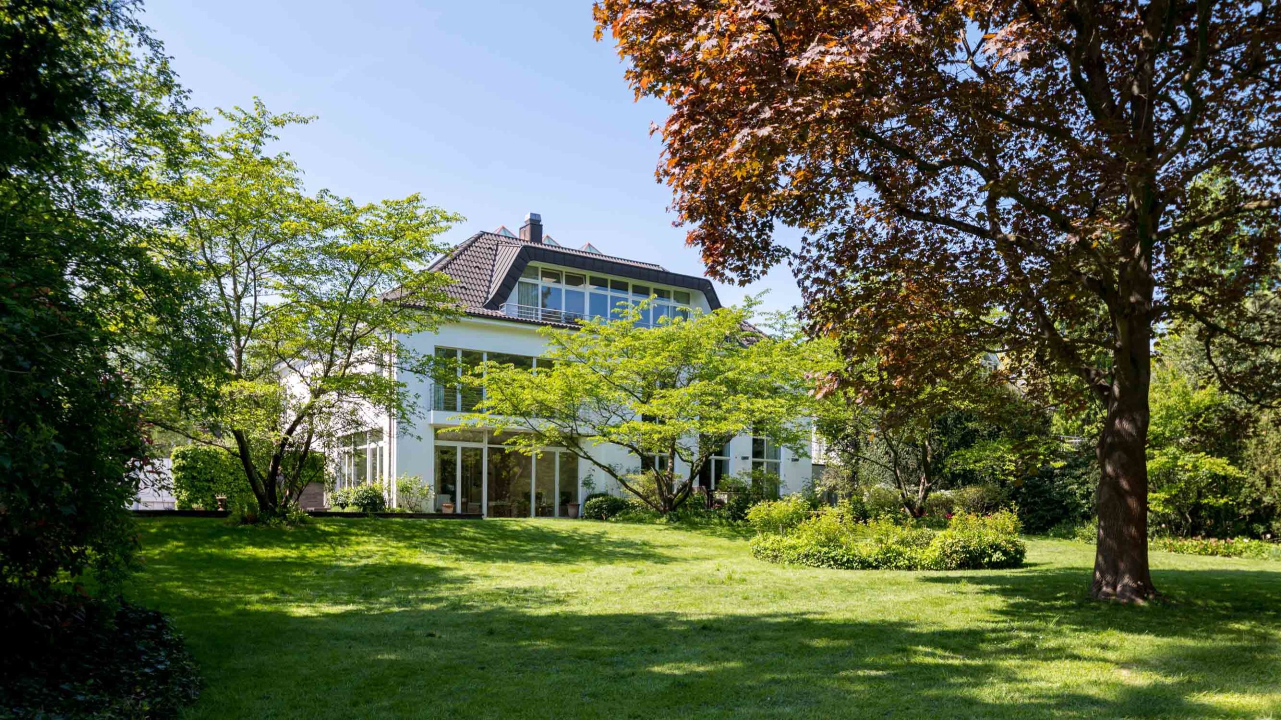 Immobilie Architekturfotografie eines Hauses in einem grünen Parkgelände. Viele Bäume und Wiesen. Foto von Immobilienfotograf Düsseldorf